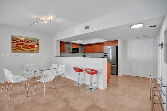 kitchen featuring light tile floors, rail lighting, a breakfast bar area, and stainless steel refrigerator with ice dispenser