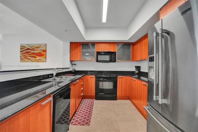 kitchen with light tile floors, dark stone counters, black appliances, a tray ceiling, and sink