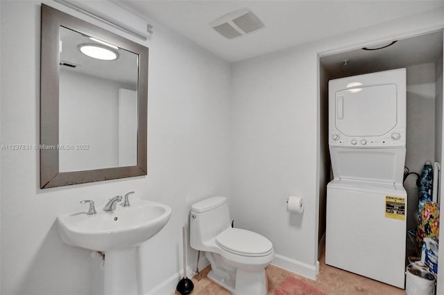 bathroom with tile flooring, toilet, and stacked washer / drying machine