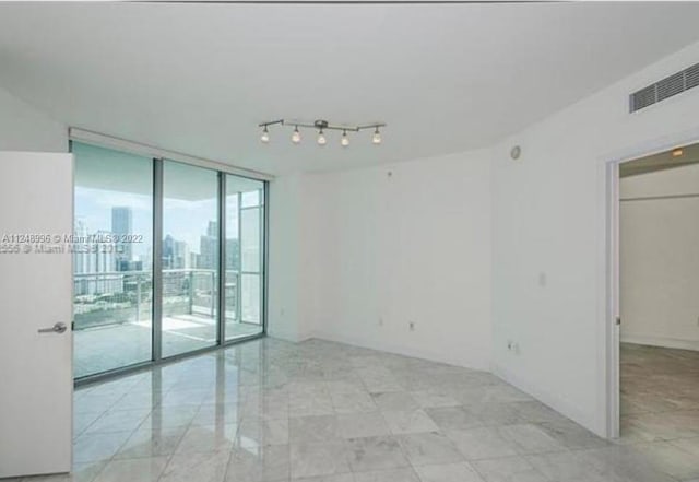 empty room featuring light tile floors, expansive windows, and rail lighting