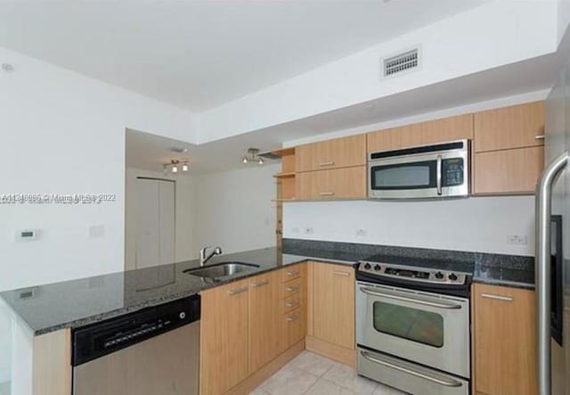 kitchen with kitchen peninsula, sink, stainless steel appliances, light tile floors, and dark stone counters