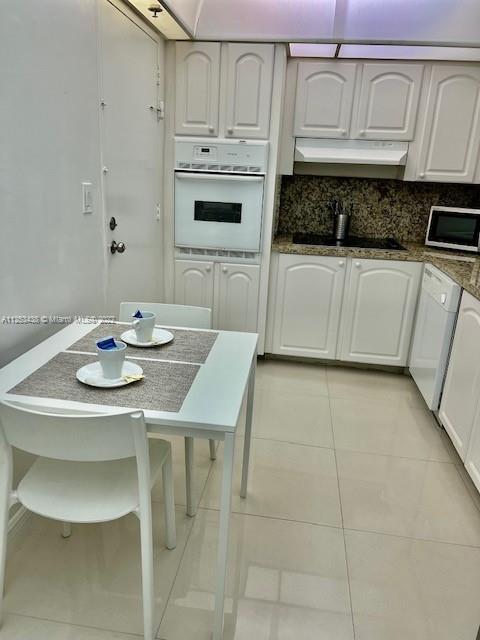 kitchen featuring light tile floors, tasteful backsplash, white appliances, and white cabinetry