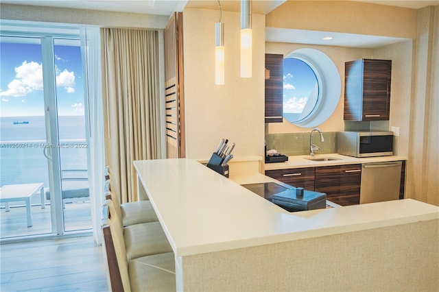 kitchen featuring decorative light fixtures, appliances with stainless steel finishes, a kitchen bar, wood-type flooring, and sink