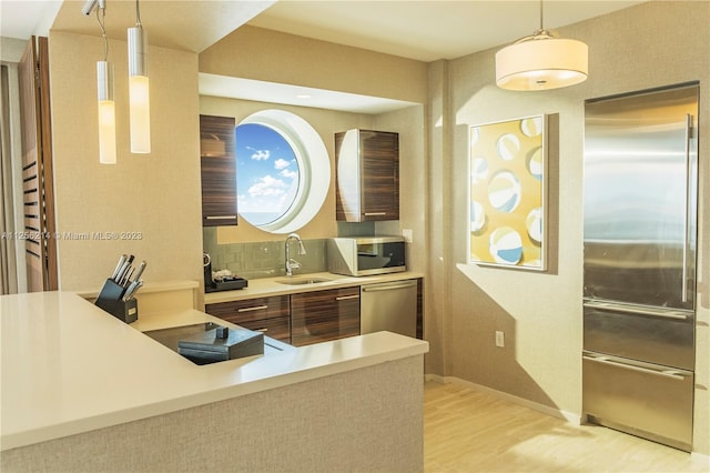 kitchen with appliances with stainless steel finishes, backsplash, hanging light fixtures, light wood-type flooring, and sink