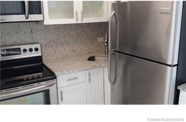 kitchen with backsplash, white cabinets, appliances with stainless steel finishes, and light stone countertops