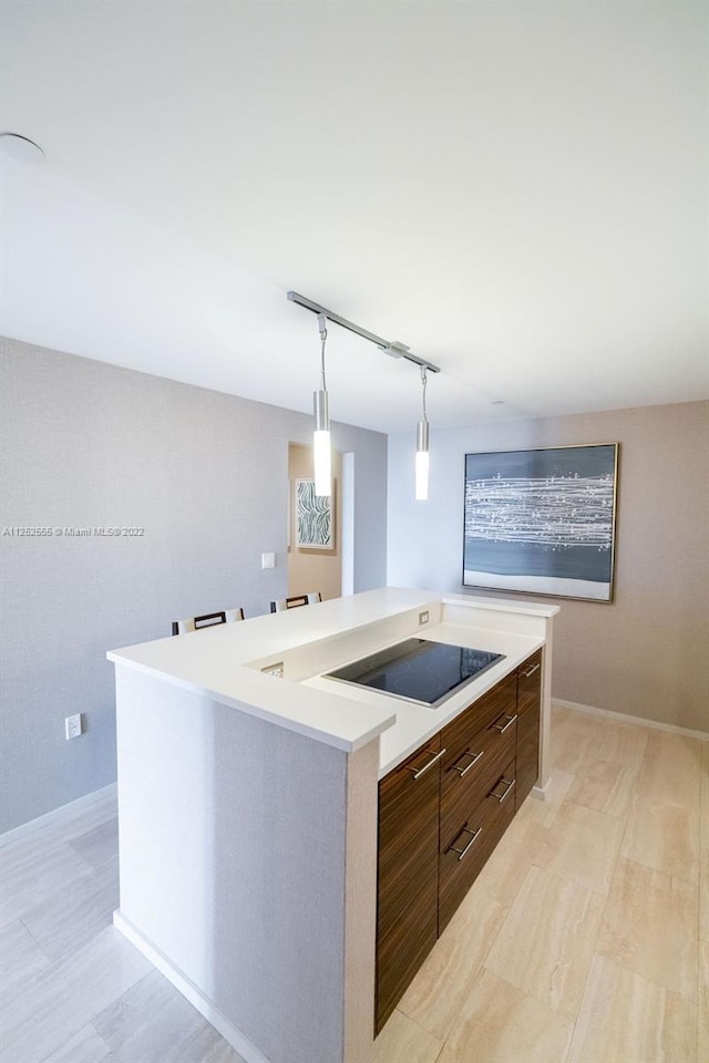 kitchen featuring decorative light fixtures, black electric stovetop, dark brown cabinets, and a kitchen island with sink