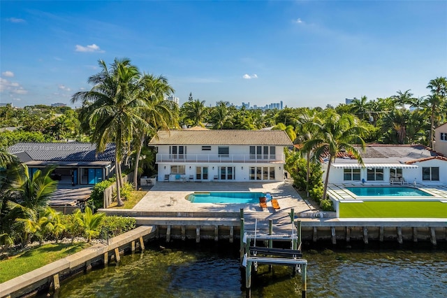 rear view of house with a swimming pool with hot tub, a patio area, and a water view