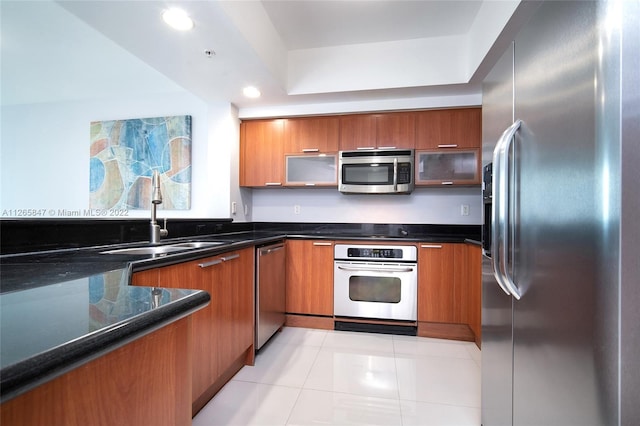 kitchen featuring light tile floors, appliances with stainless steel finishes, a raised ceiling, dark stone countertops, and sink