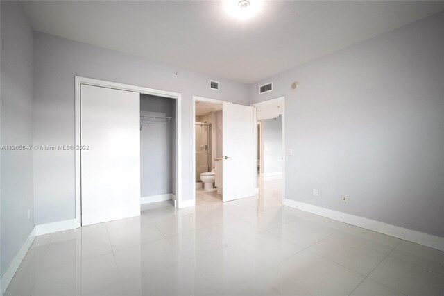 unfurnished bedroom featuring a closet, ensuite bathroom, and light tile floors