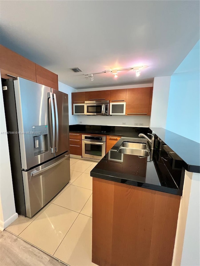 kitchen featuring stainless steel appliances, light tile flooring, kitchen peninsula, rail lighting, and sink