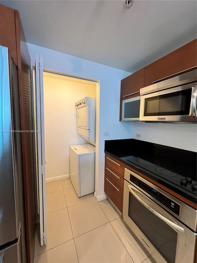 kitchen featuring light tile floors, appliances with stainless steel finishes, and stacked washer / drying machine