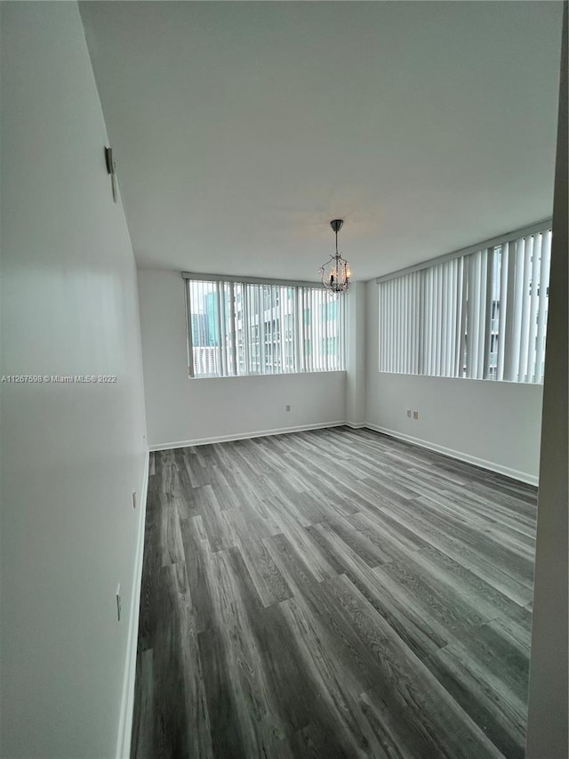 spare room with a chandelier and dark wood-type flooring