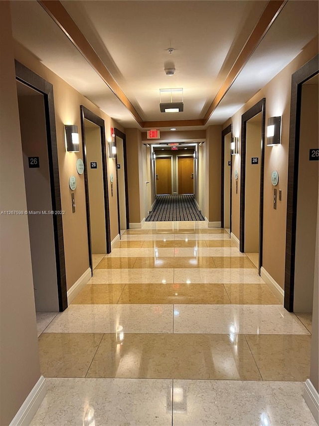 hallway with a tray ceiling, light tile floors, and elevator