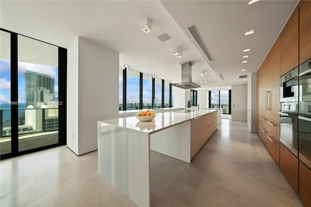 kitchen featuring light tile floors, a center island with sink, expansive windows, and island exhaust hood