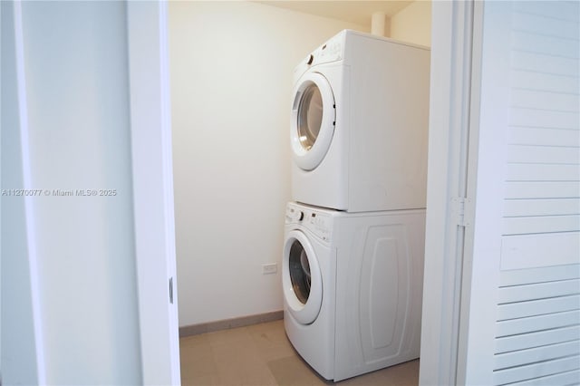 clothes washing area featuring baseboards, stacked washer / dryer, and laundry area