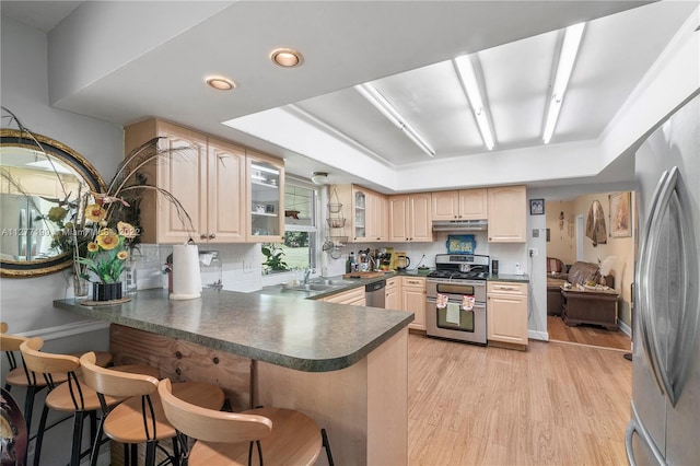 kitchen with stainless steel appliances, light hardwood / wood-style floors, kitchen peninsula, a breakfast bar area, and backsplash