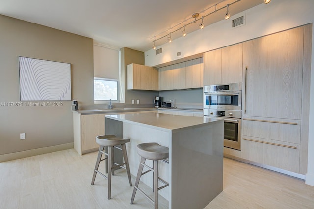 kitchen featuring double oven, a kitchen island, a kitchen bar, light brown cabinetry, and light wood-type flooring