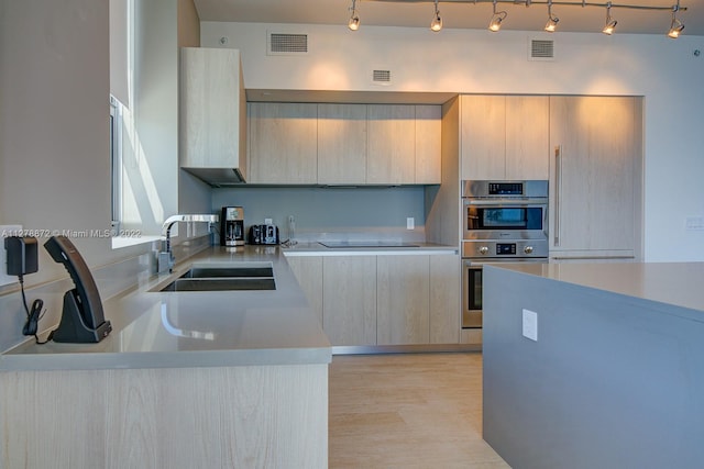 kitchen with double oven, rail lighting, light brown cabinetry, light hardwood / wood-style flooring, and sink