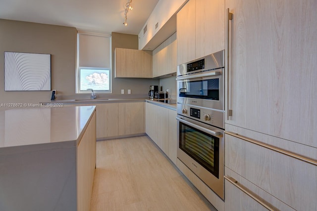 kitchen with stainless steel double oven, track lighting, light brown cabinets, sink, and light wood-type flooring