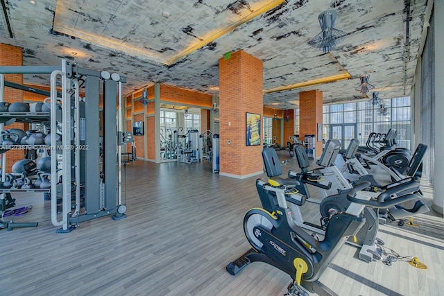 exercise room featuring brick wall, a healthy amount of sunlight, and light hardwood / wood-style flooring