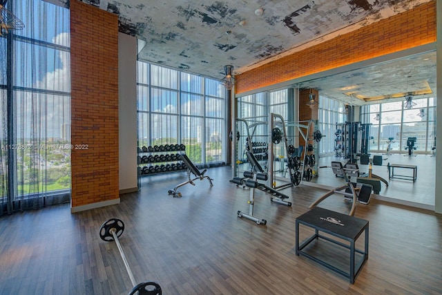 gym with brick wall, dark hardwood / wood-style floors, a wall of windows, and a high ceiling