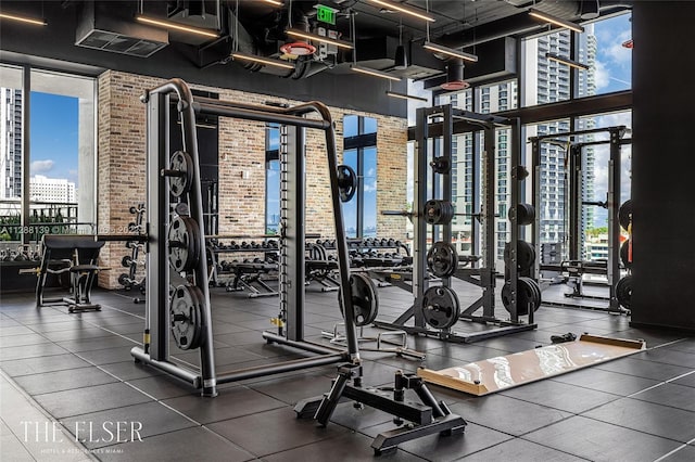 gym with a healthy amount of sunlight, floor to ceiling windows, and brick wall