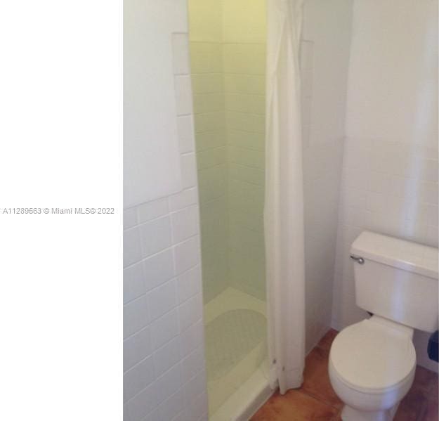 bathroom featuring tile walls, curtained shower, and toilet