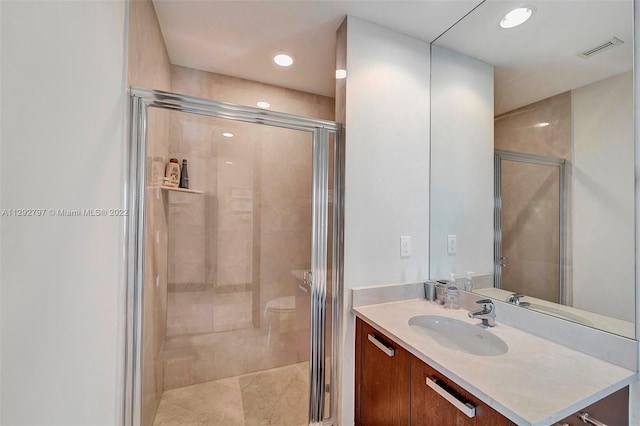 bathroom featuring toilet, vanity with extensive cabinet space, and a shower with shower door