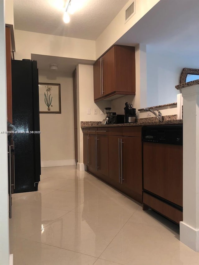 kitchen featuring dark stone counters, dark brown cabinets, stainless steel dishwasher, light tile flooring, and track lighting