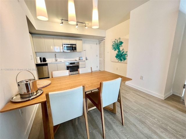 kitchen featuring stainless steel appliances, decorative light fixtures, sink, light wood-type flooring, and track lighting