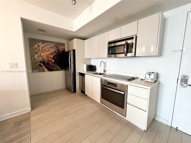 kitchen featuring stainless steel appliances, light wood-type flooring, white cabinets, and sink