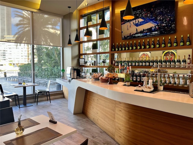 bar with floor to ceiling windows, light hardwood / wood-style floors, pendant lighting, and a wealth of natural light