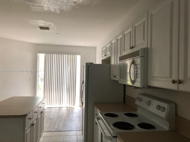 kitchen with white appliances, white cabinets, a textured ceiling, and light tile flooring