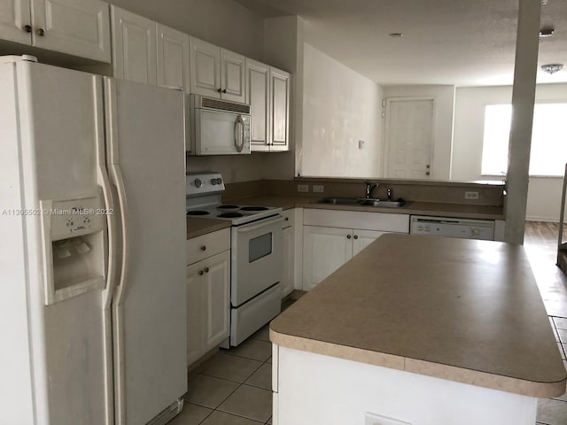 kitchen with white appliances, sink, light tile floors, a kitchen island, and white cabinets