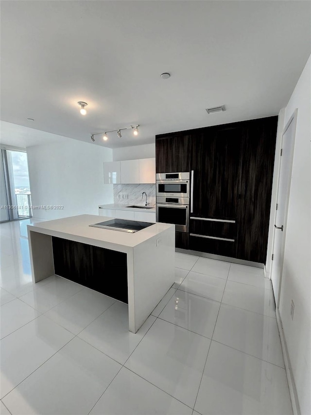 kitchen with a center island with sink, rail lighting, double oven, and light tile flooring