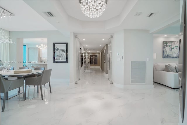 hall with a tray ceiling, light tile floors, and a notable chandelier