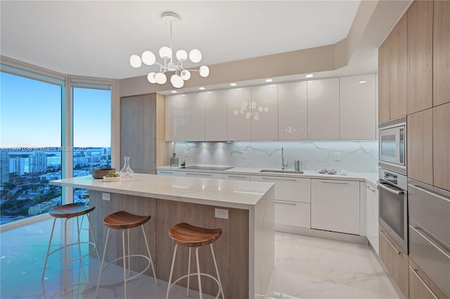 kitchen featuring stainless steel appliances, a notable chandelier, a center island, a breakfast bar, and white cabinetry