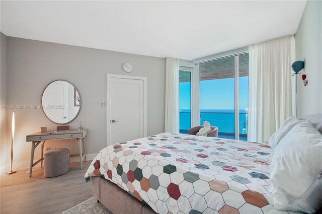 bedroom with a water view, access to exterior, and light hardwood / wood-style flooring