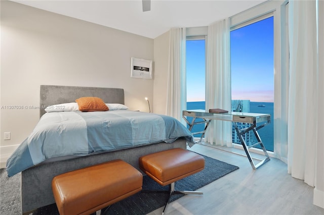 bedroom with a water view, floor to ceiling windows, light hardwood / wood-style floors, and ceiling fan