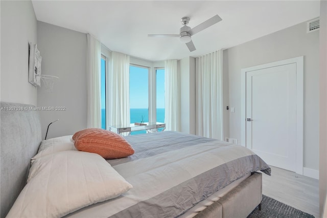 bedroom with a water view, light hardwood / wood-style floors, and ceiling fan