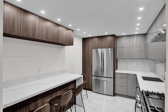 kitchen featuring stainless steel fridge, a breakfast bar area, sink, and light stone counters