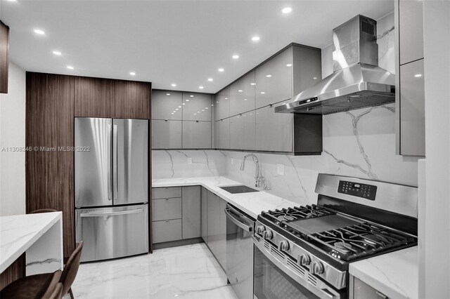 kitchen featuring gray cabinetry, wall chimney exhaust hood, light stone counters, and stainless steel appliances