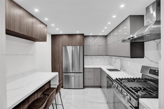 kitchen with a kitchen breakfast bar, stainless steel appliances, wall chimney range hood, light stone countertops, and sink