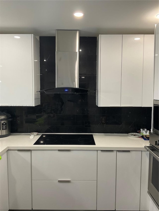 kitchen with oven, white cabinetry, backsplash, and wall chimney range hood