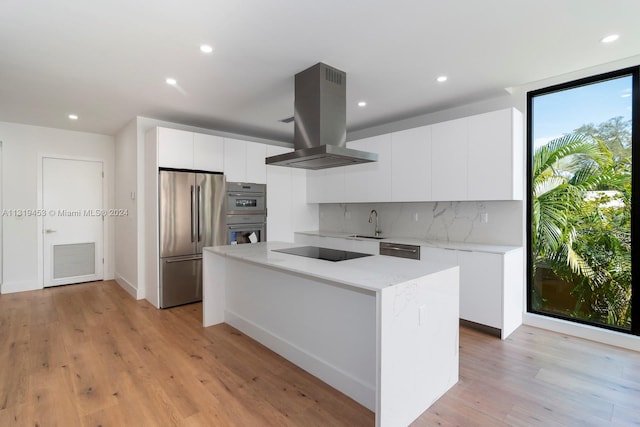 kitchen with island range hood, stainless steel appliances, white cabinets, backsplash, and light wood-type flooring