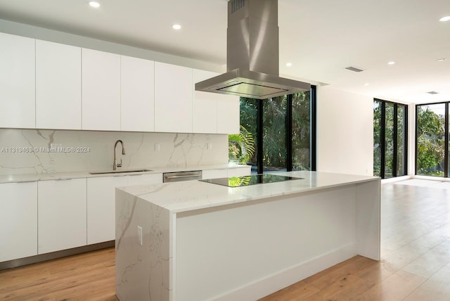 kitchen featuring island range hood, expansive windows, white cabinetry, backsplash, and light stone counters