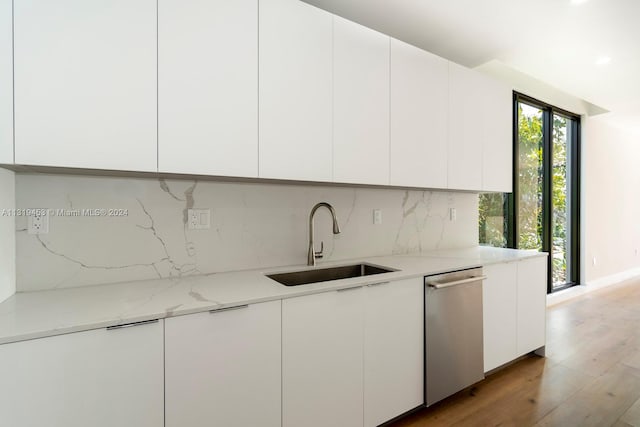 kitchen featuring light stone countertops, light hardwood / wood-style flooring, white cabinetry, dishwasher, and sink