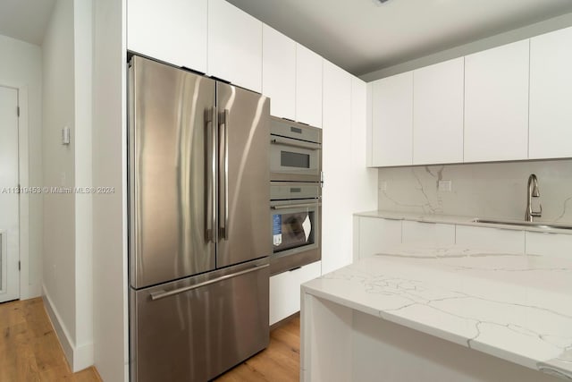 kitchen with light stone counters, stainless steel appliances, tasteful backsplash, white cabinetry, and light wood-type flooring