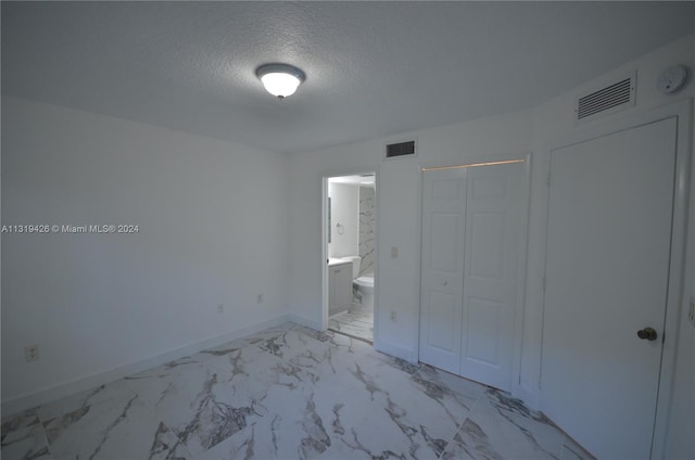 unfurnished bedroom featuring connected bathroom, a closet, and a textured ceiling