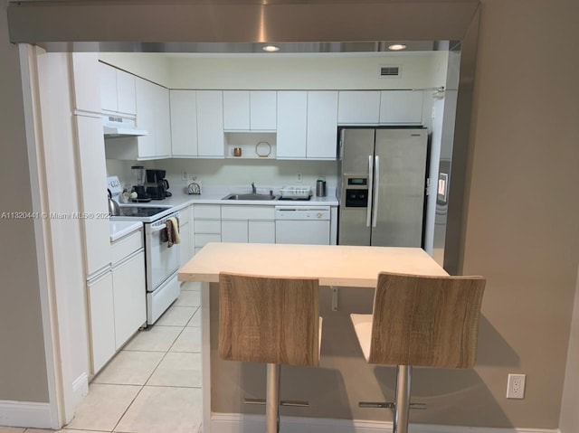 kitchen featuring white appliances, a kitchen bar, sink, light tile floors, and white cabinets